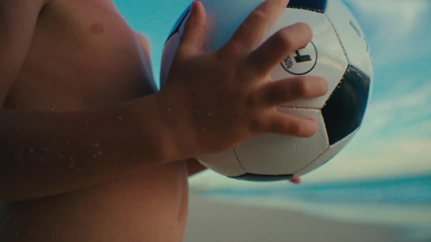 Boy on the beach without a shirt holding a soccer ball