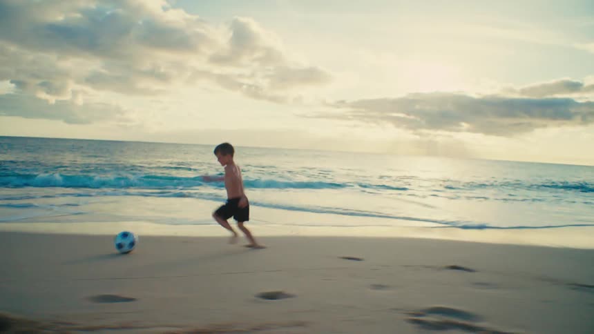 A boy playing football alone on the beach during the day