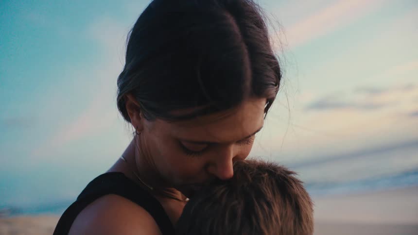 Mother hugging her little son and giving him kisses in a beach setting