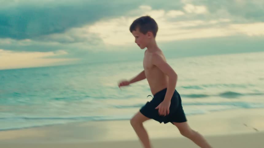 Young boy runs while kicking a soccer ball across the beach during daytime