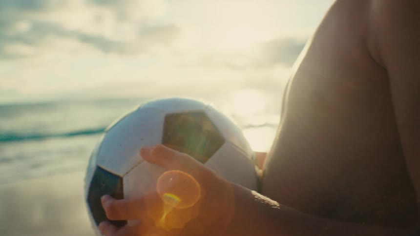 A person holds a soccer ball as waves crash in the distance