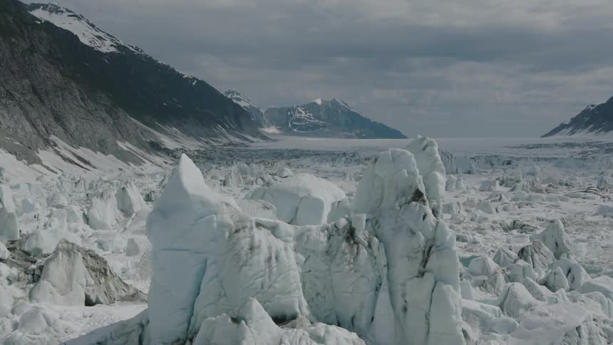 Aerial view of Alaska with vast icy glacier surrounded by rugged mountains and cloudy skies