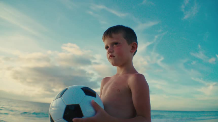 Shirtless boy on the beach holding a soccer ball