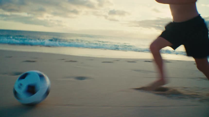 Boy playing soccer alone on a beach in the late afternoon