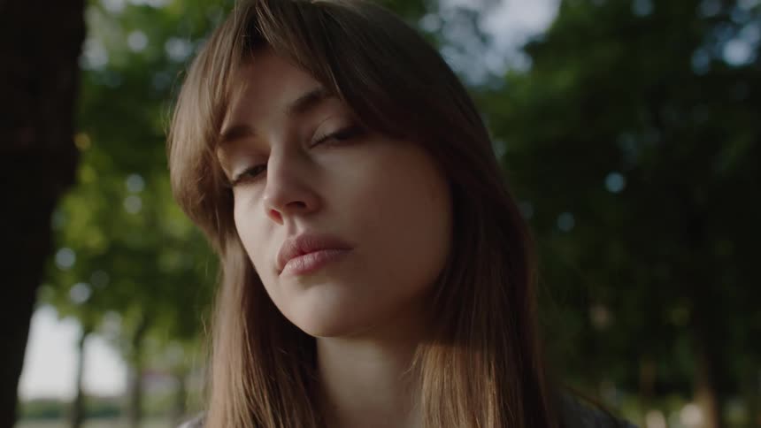 A young woman stands in a forest facing the camera with a calm look