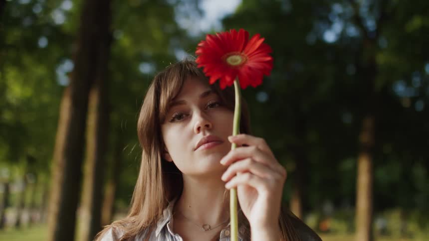 Woman in a forest during the day holding an orange flower