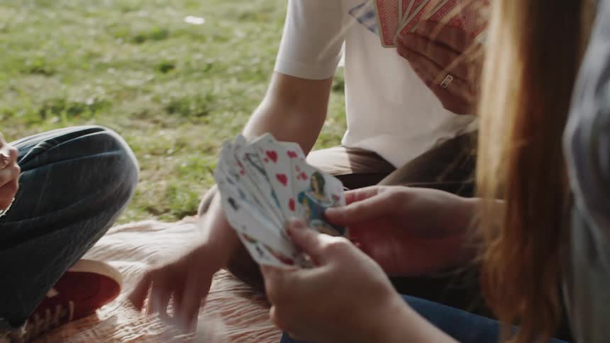 Three people sitting outdoors on the grass playing cards