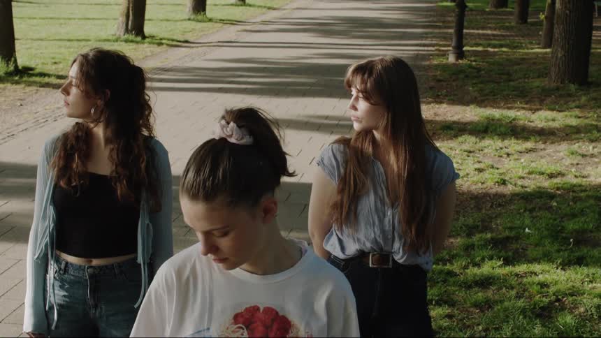 Three young women stand in a park looking away in quiet thought