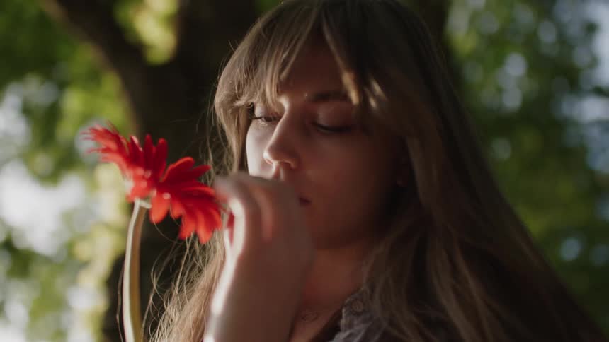 The woman is touching and examining a red flower