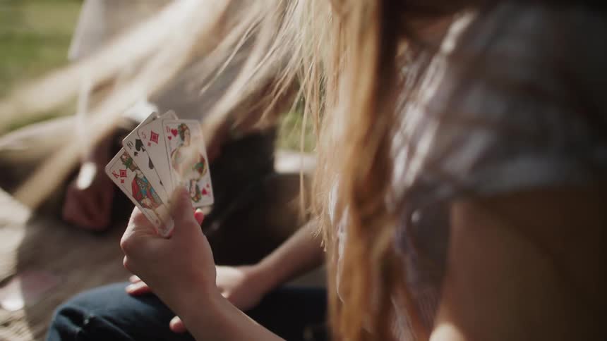 Three kids sit on a mat in a park playing a card game