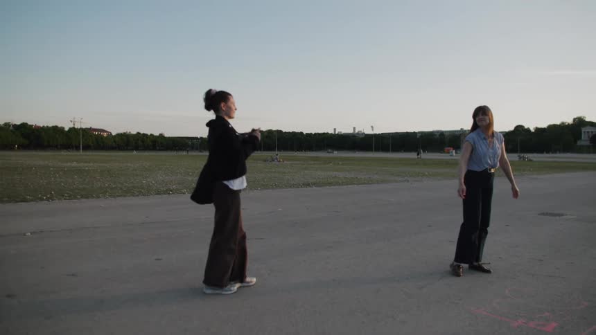 A woman poses as another takes her photo outdoors during golden hour