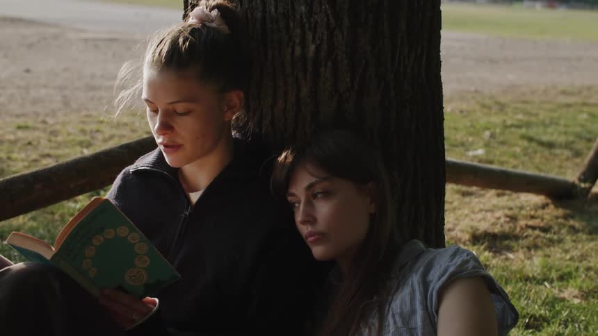 Two ladies sitting under a tree in the evening with one reading a book