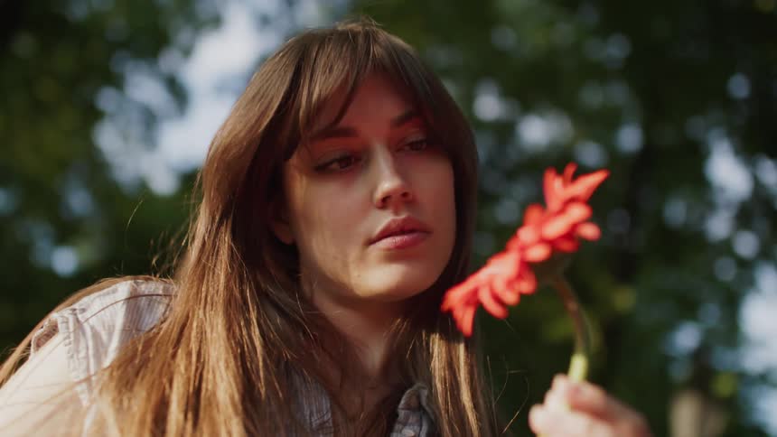 A young woman holds flowers in a public park at midday continuously staring at them