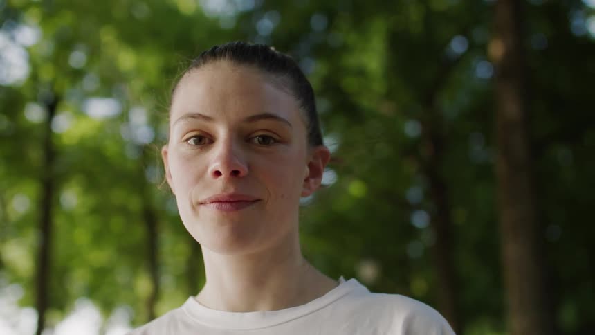 A young woman smiles calmly at the camera in a sunlit forest
