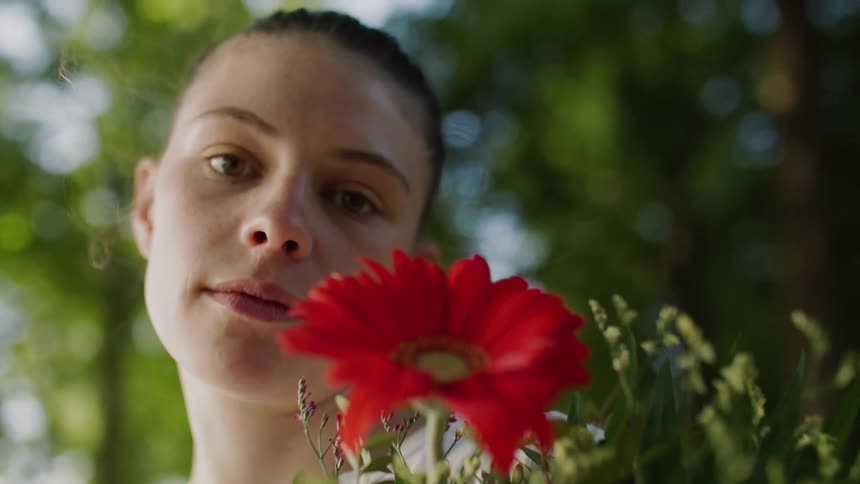 Woman outdoors surrounded by trees holding a flower