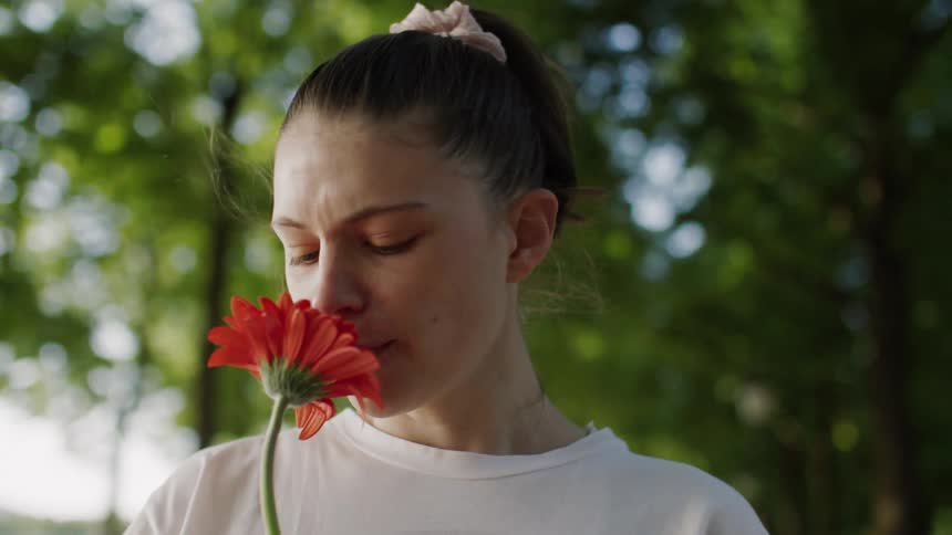 A girl sniffs a flower in the woods