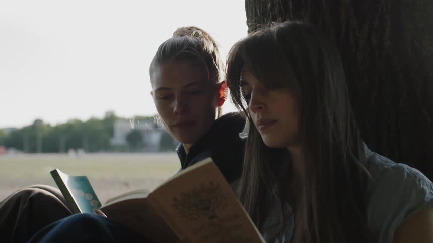 Two females sitting outside against a tree are reading books