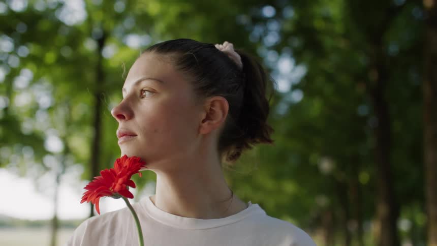 Woman holding a flower while standing in a treelined environment