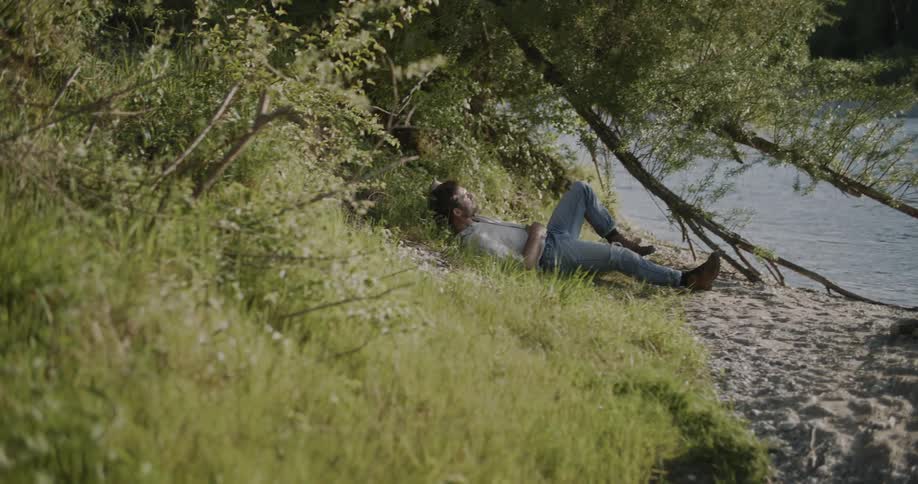 The man lays back on the side of the river