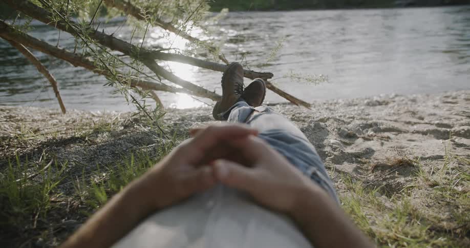 A man is laying in the grass by the stream