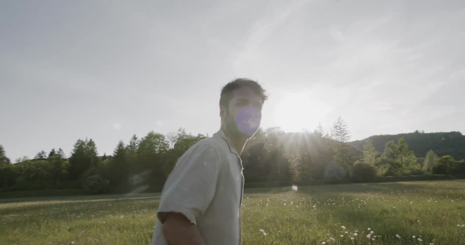 Man standing in a sunlit meadow holding a flower and enjoying the moment