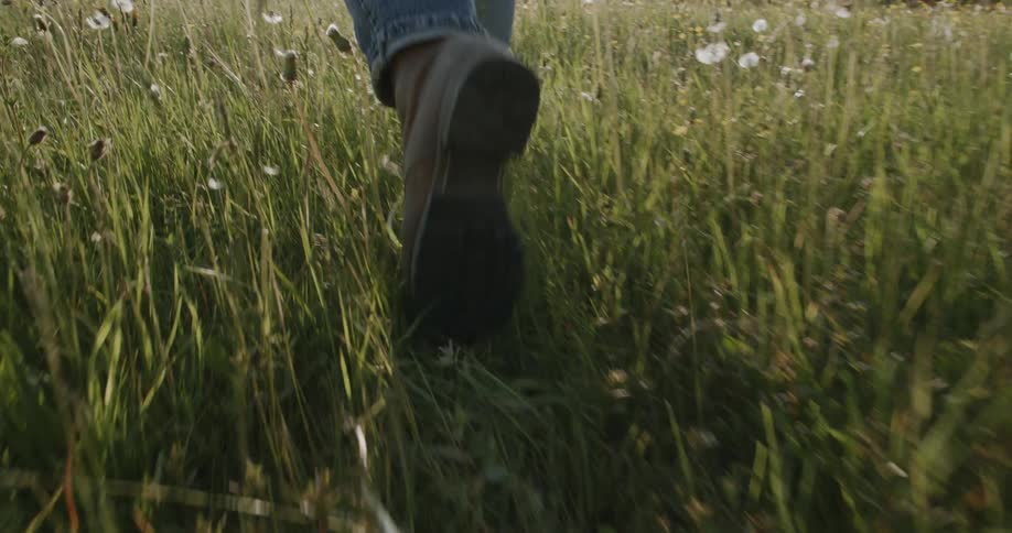 Person wearing boots walks through a grassy field