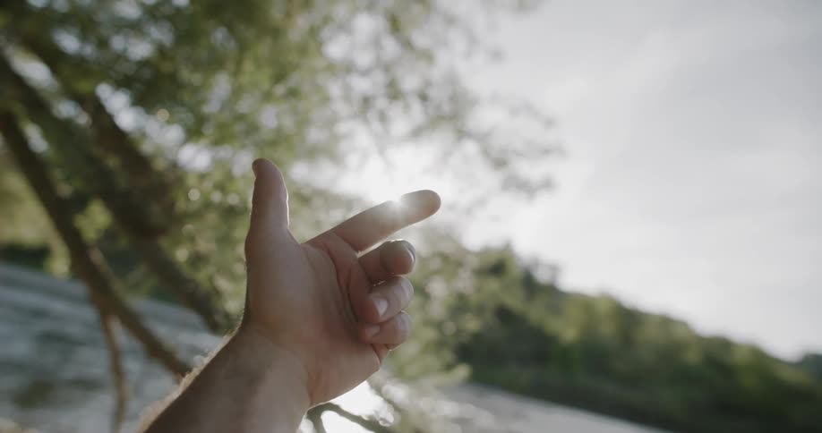 A hand waving in the air outdoors near a river