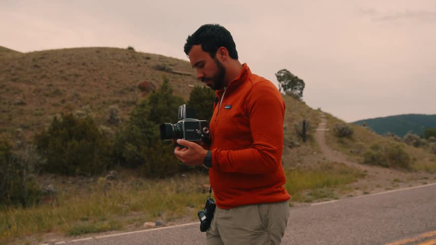 Male filmmaker on a road surrounded by mountains carrying a professional video camera