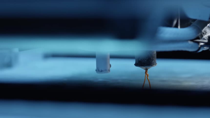 3d printer extruder nozzle deposits orange filament onto the bed during printing