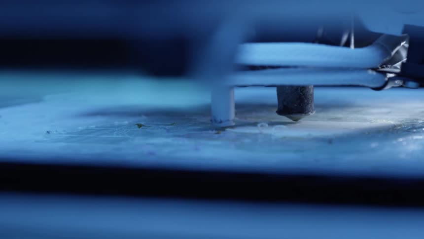 3d printer nozzle deposits layers of material on surface illuminated by blue light