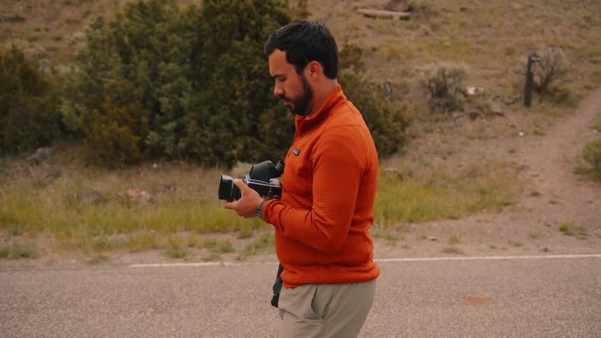 Man in orange jacket takes photo with vintage camera by rural roadside