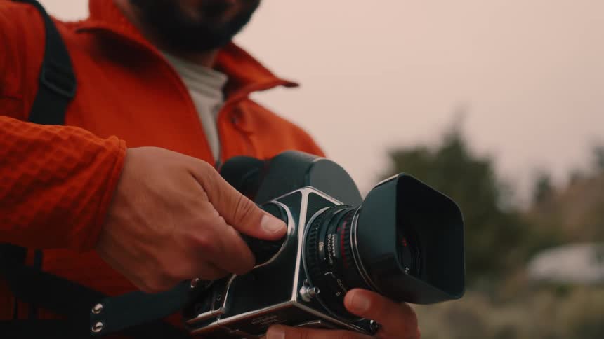 A man wearing a red sweatshirt holds a mediumformat film camera inserts a dark slide and then tries to take a shot