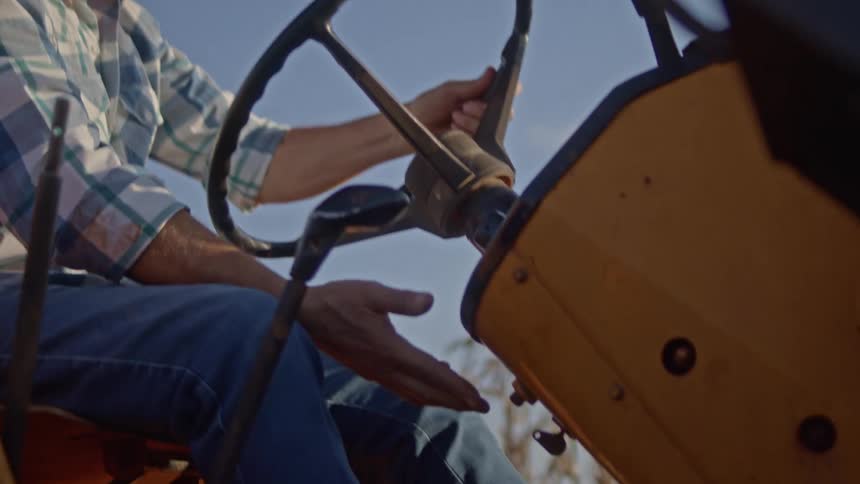 Male farmer pushes a button below the steering wheel while sitting in a farm tractor during daytime