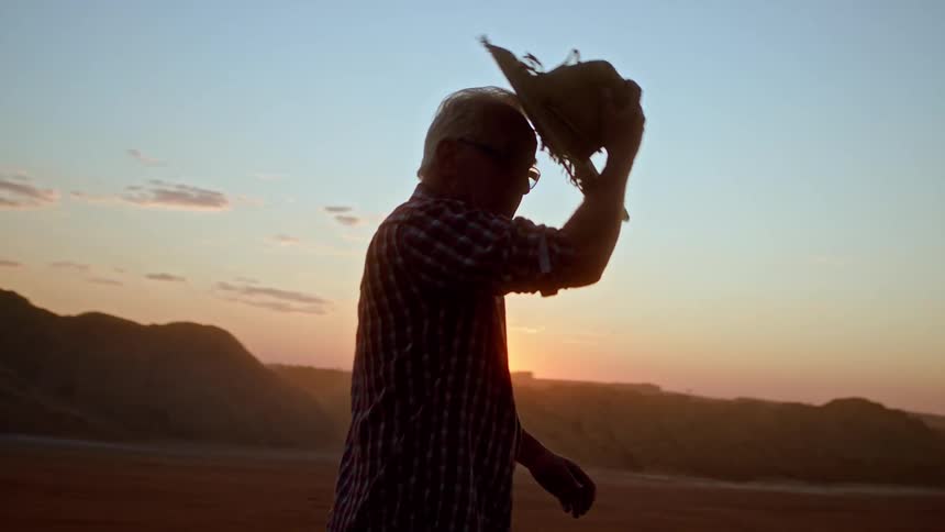 Man puts on a cowboy hat as he walks through the desert