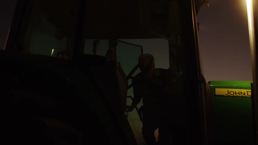 Male farmer climbs into a green farm tractor outdoors at night