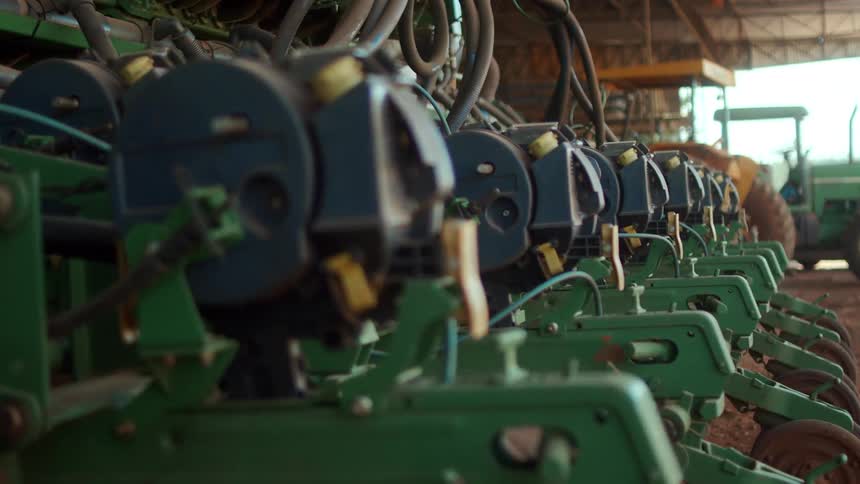 A row of green agricultural machinery is lined up inside a barn or shed