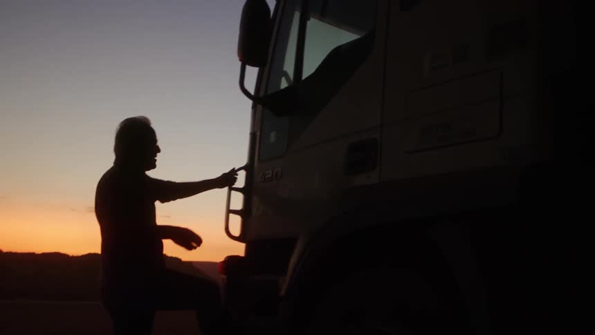 A person is silhouetted against a colorful sunset stepping into a large truck