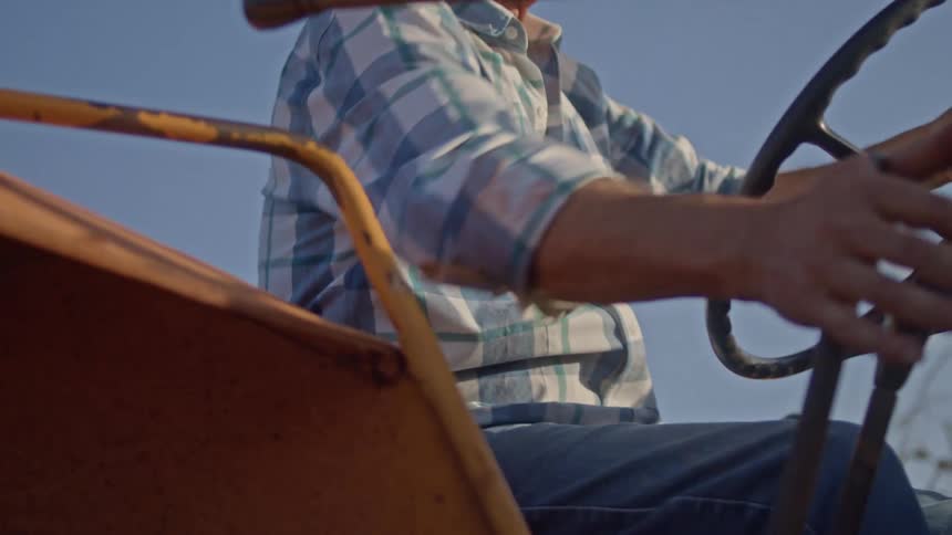 An elderly man wearing a straw hat is operating a vehicle outdoors