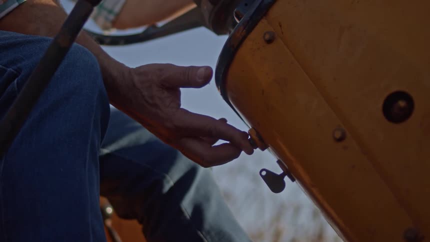 A person seated in a yellow tractor pushes the start button and then operates the pedals