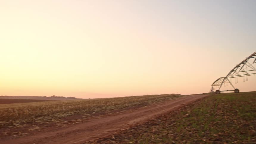 A man stands under some farm equipment as shot reveals the sunsetsunrise