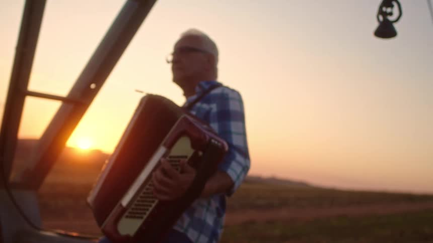 Elderly man with glasses sitting playing accordion