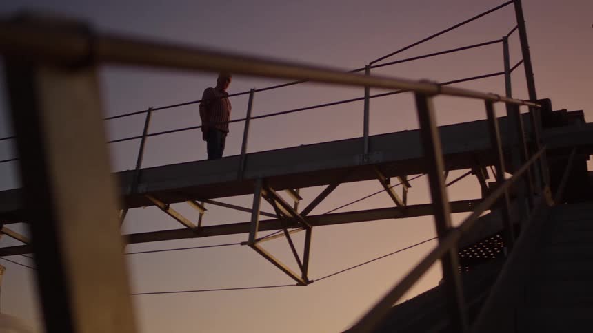 A man walks on a steel pedestrian bridge at sunset