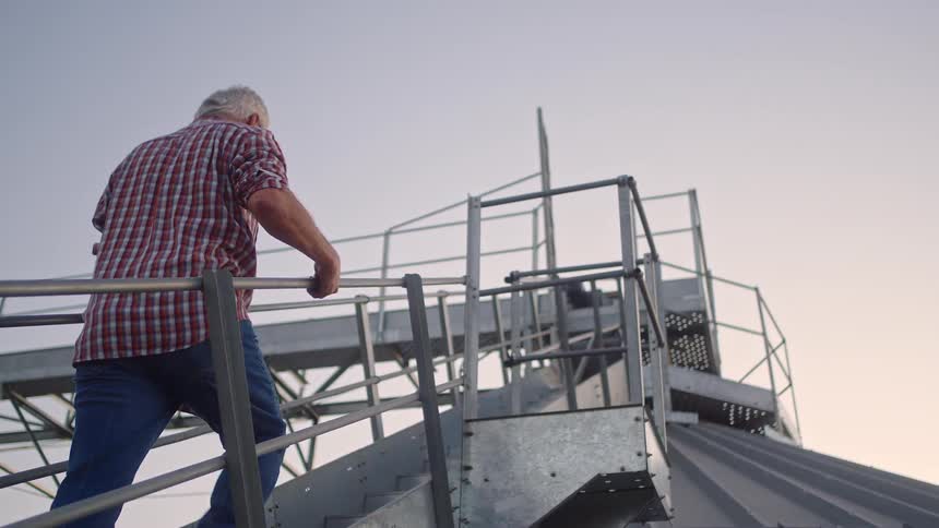 Man in red plaid shirt ascends a set of metal steps attach to a metal dome at duskdawn