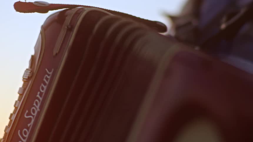 Person plays red accordion with white details illuminated by evening light