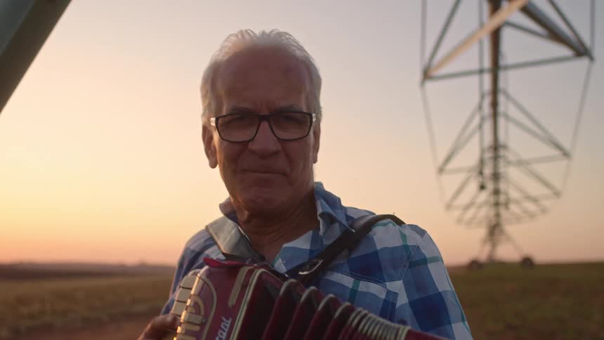 The man plays the accordion while smiling at sunrise