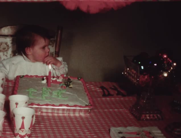 A baby is sitting by a birthday cake