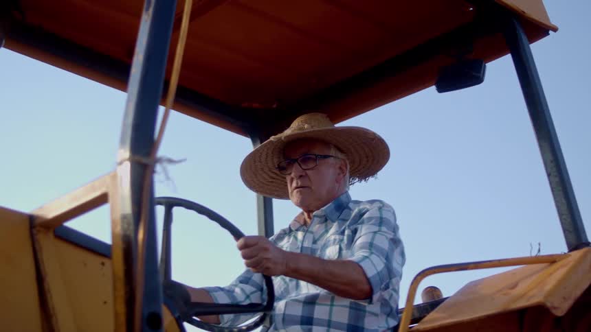 A male farmer drives and steers a farm tractor on a farm during daytime