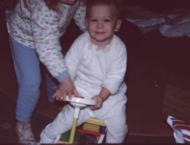 An older film of a child riding around on a toy in the house