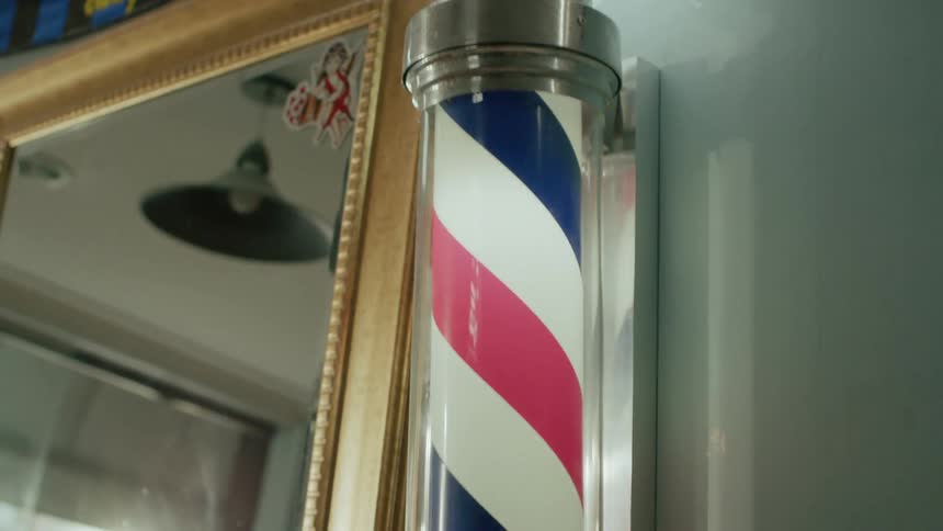 A classic red white and blue barber pole is mounted on a wall next to a goldframed mirror inside a barbershop