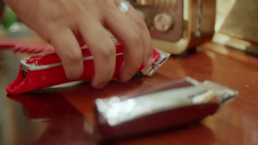 Close up of a male barbers hand as he picks up a red hair clipper from a tabletop in a salon
